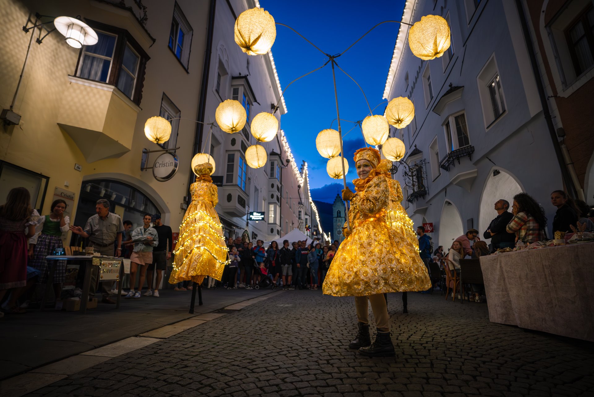 Stelzenfiguren unter Laternen in der abendlichen Neustadt