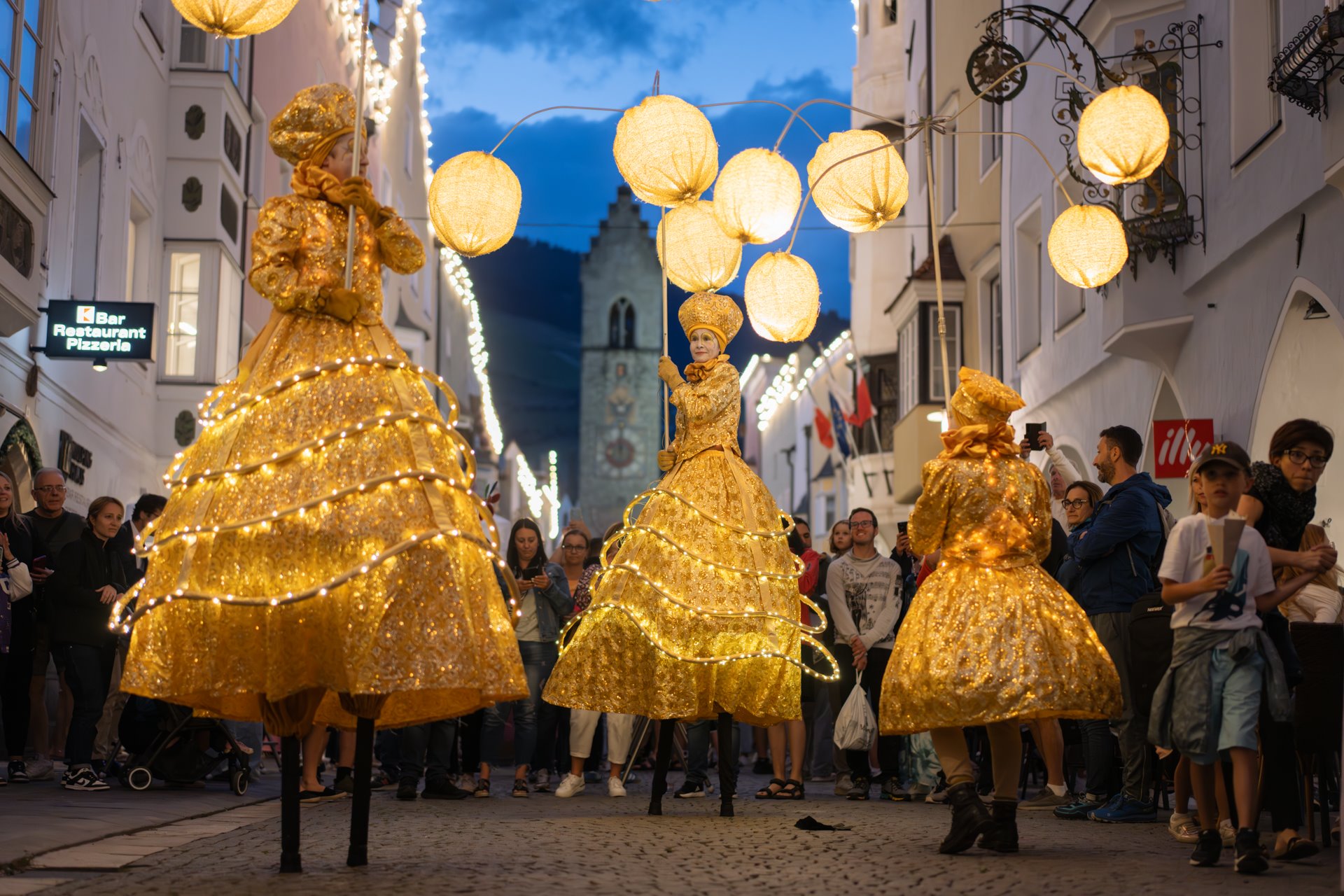 Stelzenfiguren in goldenen Kostümen vor Publikum